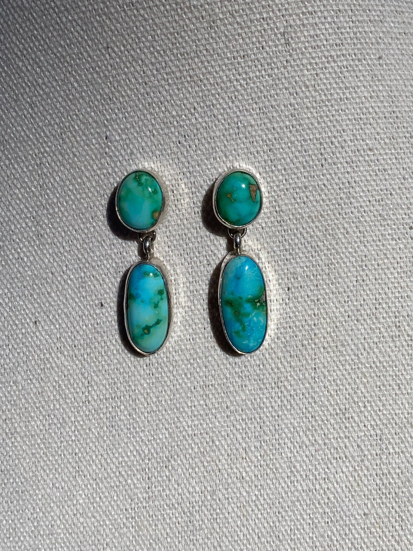 Sonoran turquoise dangle earrings with two-stone design in sterling silver on a cream display